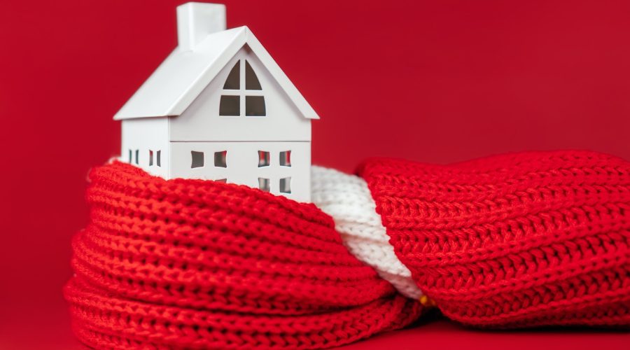 White toy house wrapped in red scarf on red background. Heating or insulating buildings or houses